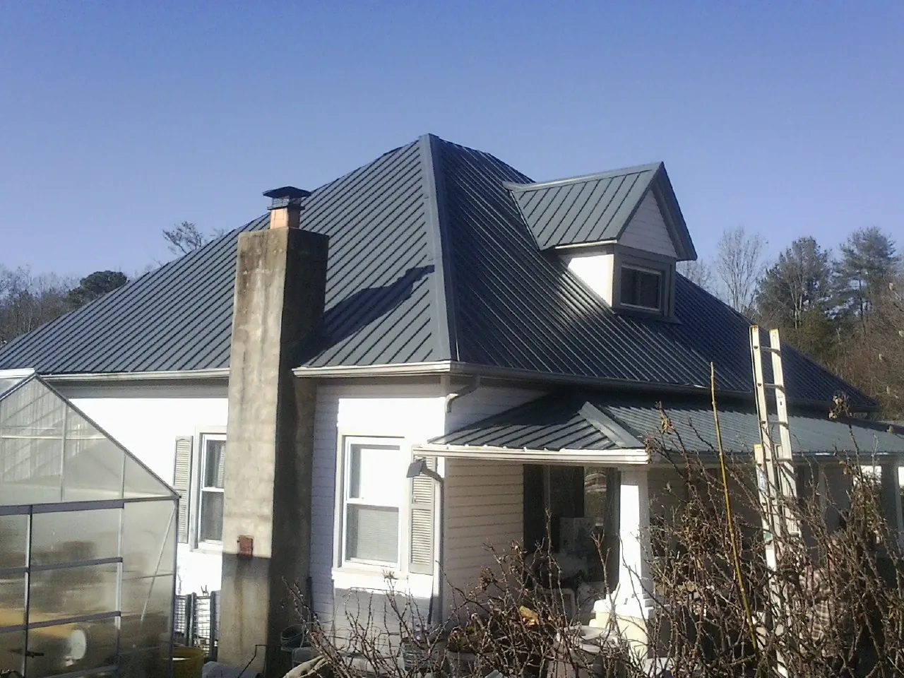 Dark blue standing seam metal roof on a white farmhouse with dormer — Slate & Tile Roof Repair by Roofing Brothers in Basile