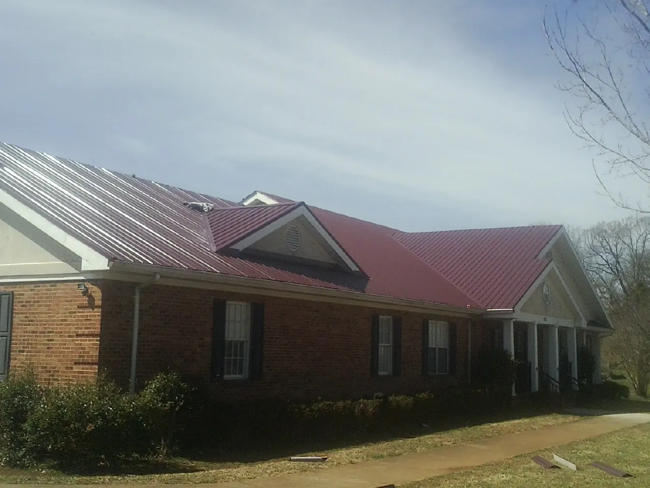 Red metal roof with gabled entries on a long brick building, from a Hail Damage Roof Repair job in Basile