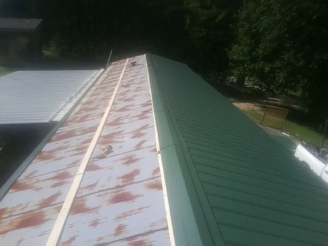 Old rusted panels beside newly installed green metal roofing — Wind Damage Roof Repair by Roofing Brothers in Basile