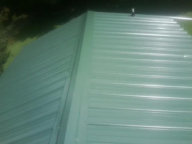 New green metal panels meeting at the ridge of a roof — Flat Roof Repair work by our crew in Basile