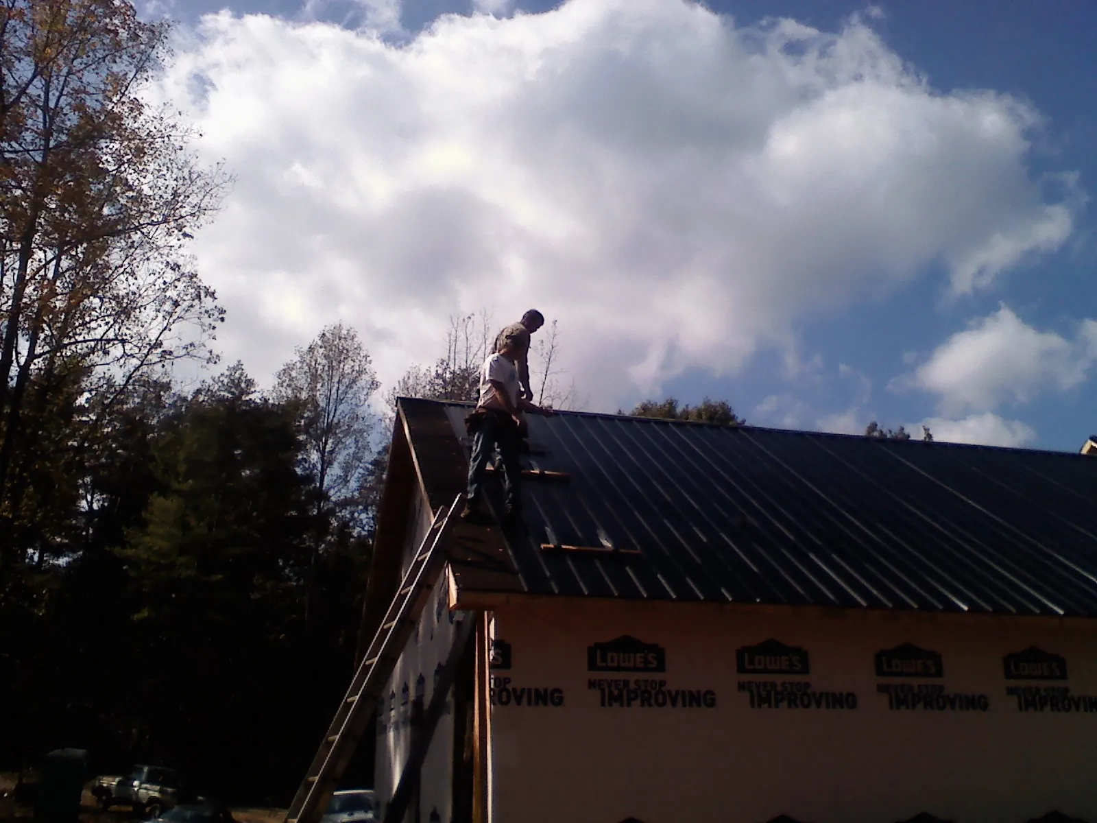 Roofer fastening dark metal panels high against a cloudy sky, from a Roof Inspection job in Basile