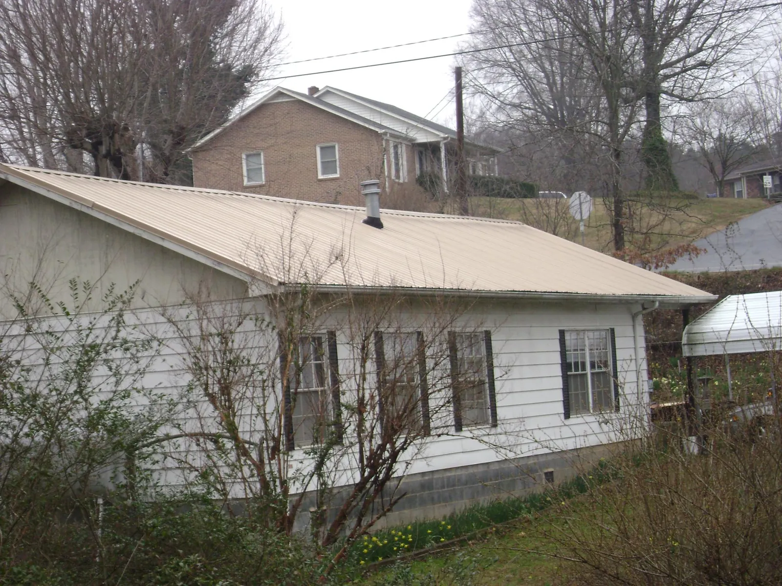 Tan metal roof on a white sided house set into a hillside — Commercial Roofing by Roofing Brothers in Basile