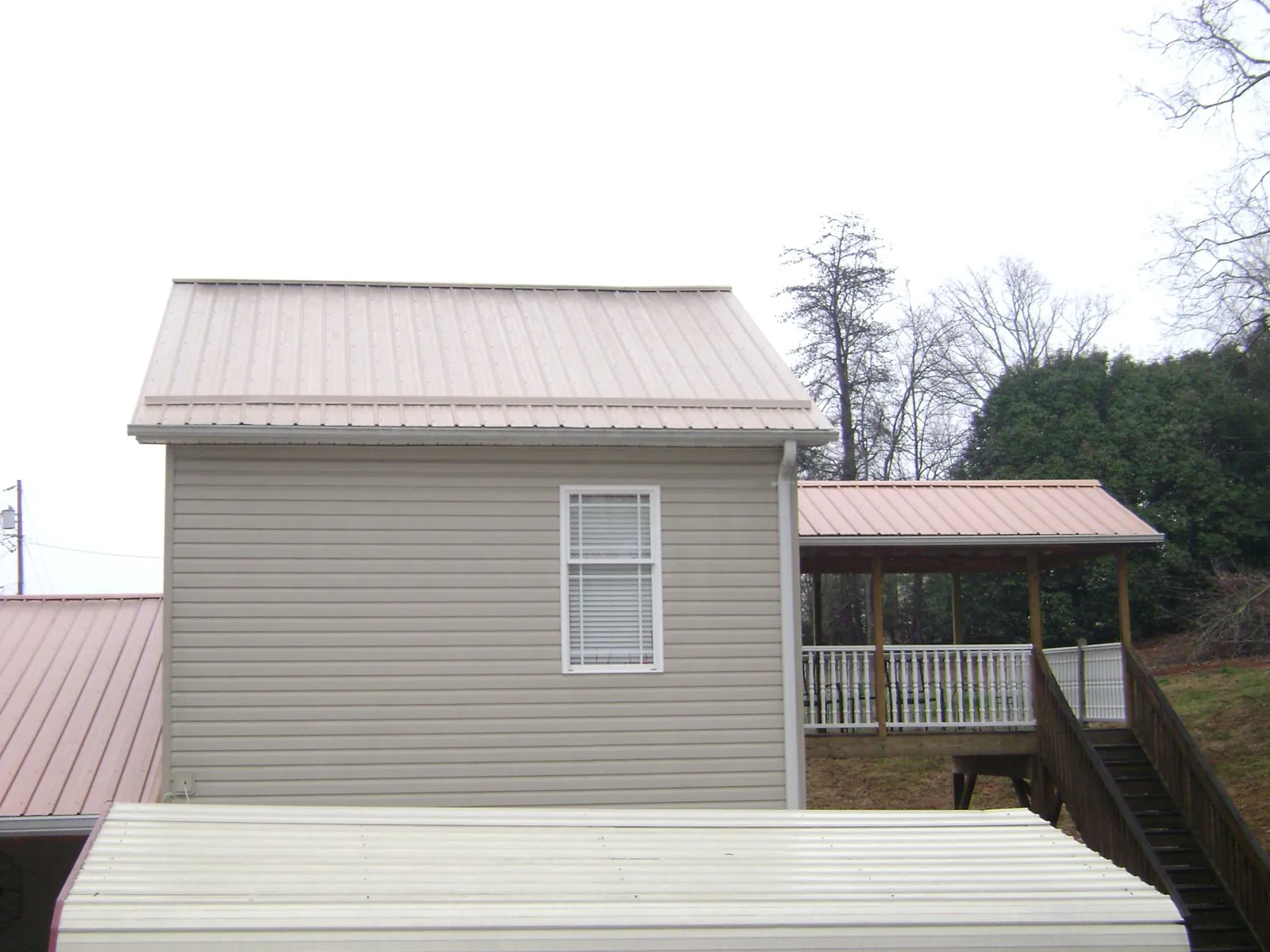 Tan metal roofs on a two story addition and attached porch, from a Roof Replacement job in Basile